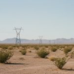 Flat Arizona desert scrubland with a line of steel electricity transmission towers running toward bare hills on the horizon.