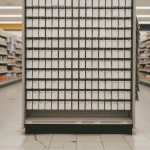 A supermarket end-cap rack filled with rows of identical blank white gift cards hanging on metal pegs, flanked by stocked grocery shelves under fluorescent light.