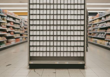 A supermarket end-cap rack filled with rows of identical blank white gift cards hanging on metal pegs, flanked by stocked grocery shelves under fluorescent light.